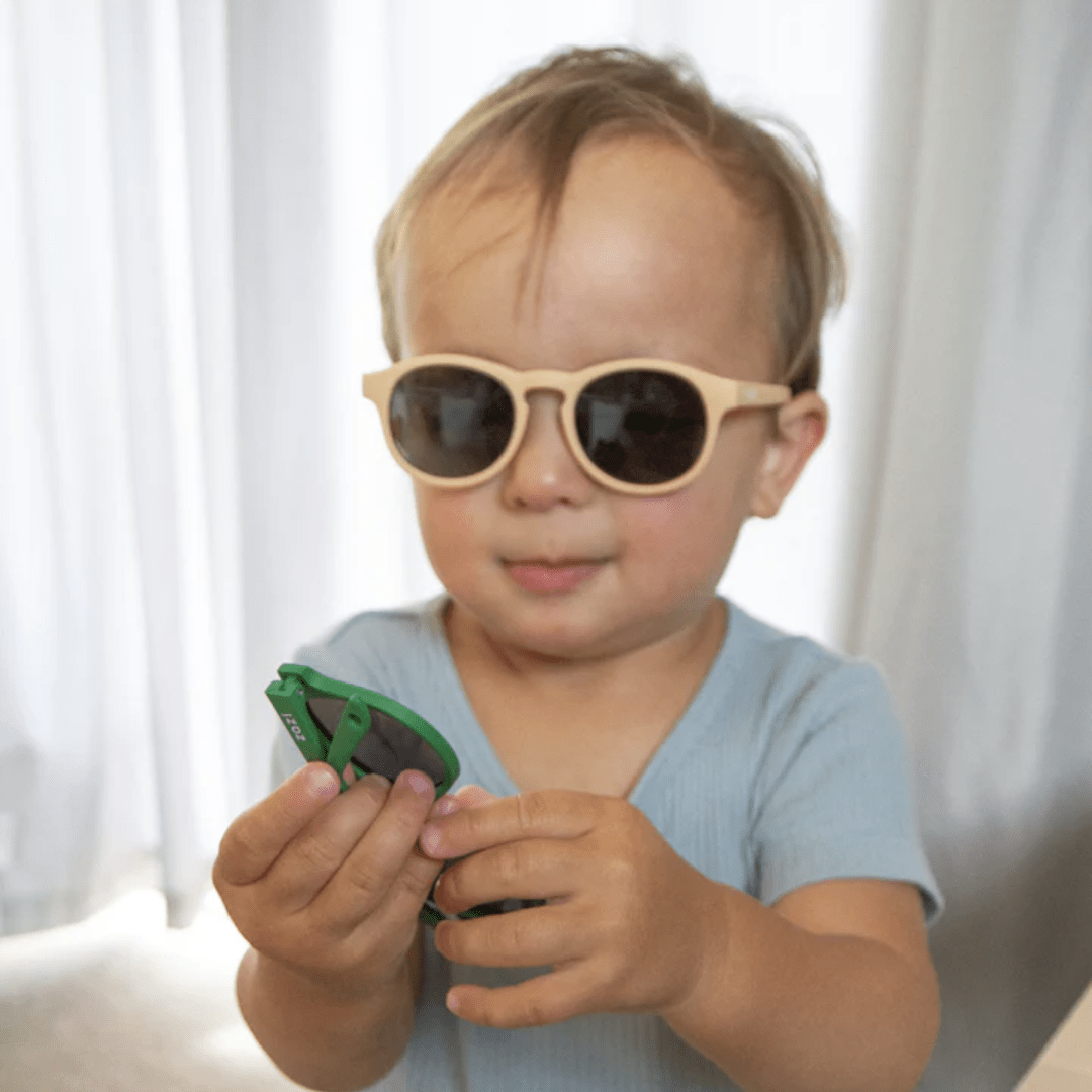 A young boy wearing Zazi Shades Baby & Toddler Sunglasses and holding a cell phone.