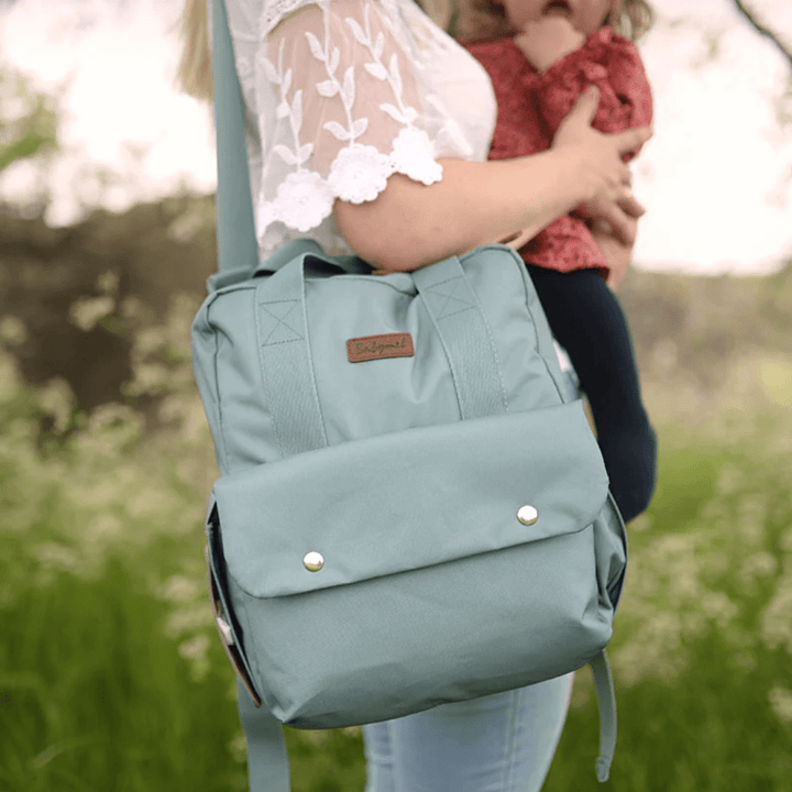 Mum-in-Field-Holding-Baby-Wearing-Babymel-Georgi-Eco-Convertible-Nappy-Backpack-Aqua-As-A-Shoulder-Bag-Naked-Baby-Eco-Boutique
