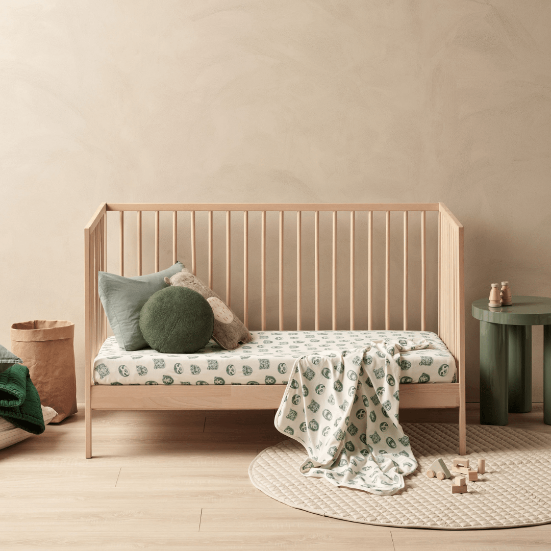 A crib with the Wilson & Frenchy Organic Cotton Cot Sheet - LUCKY LASTS - FLOAT AWAY ONLY and a round rug, perfect for a baby shower present.