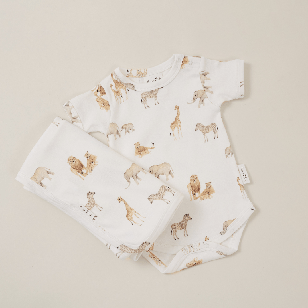 An Aster & Oak organic cotton baby bodysuit with a hand-illustrated print of giraffes and elephants.