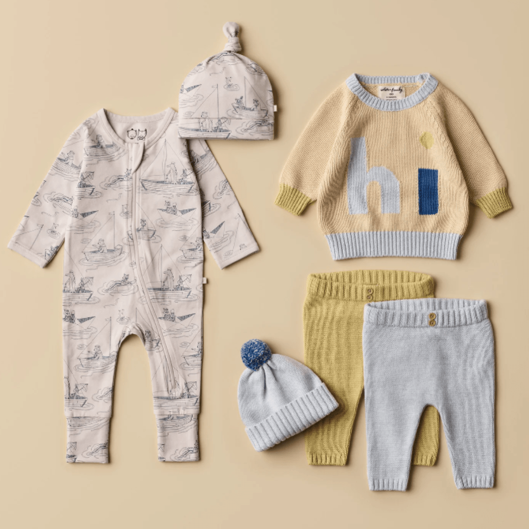 A collection of baby clothing including a patterned onesie, a Wilson & Frenchy Knitted Jacquard Jumper with the word "hi," and a pair of pants and leggings, all displayed on a beige background.