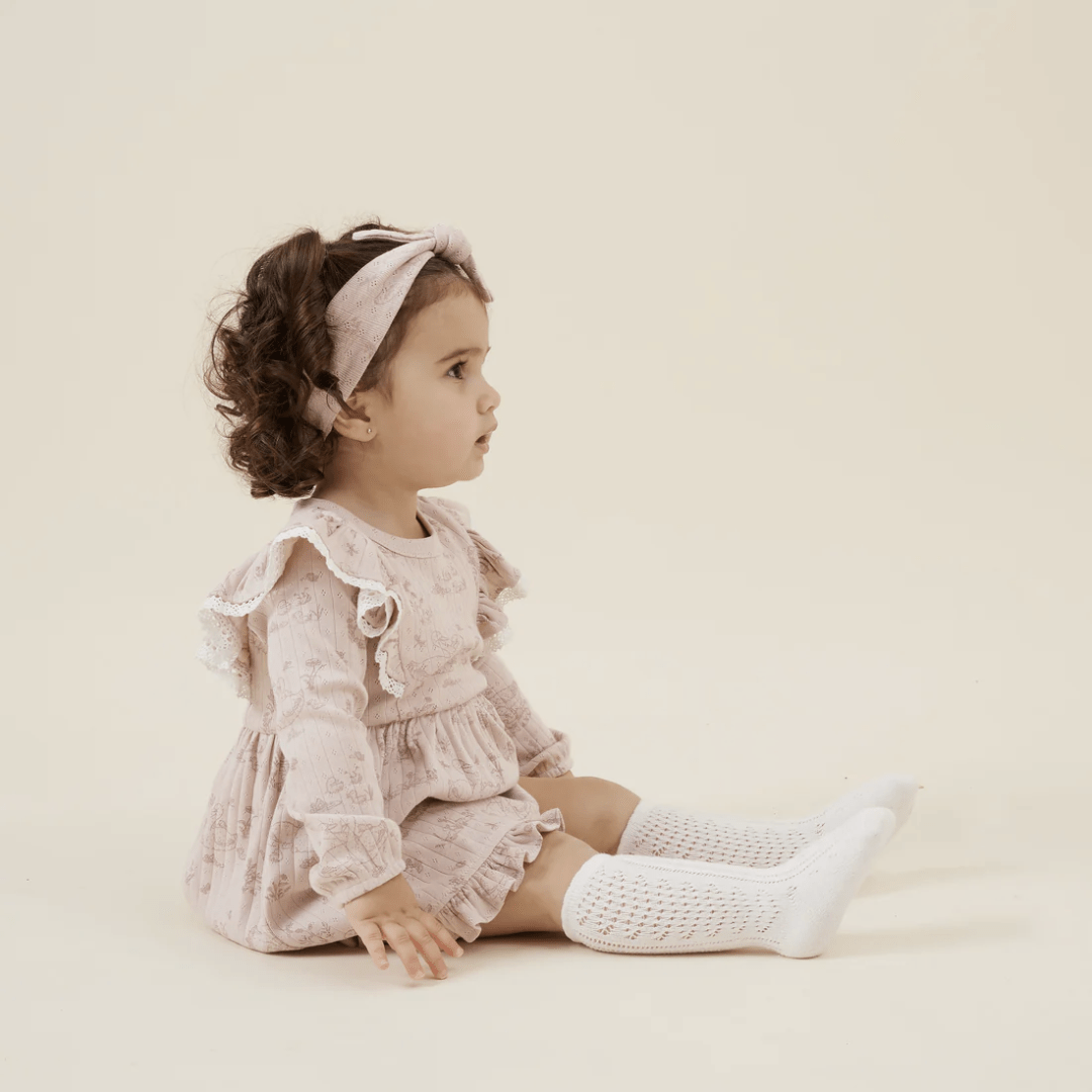 Side-Veiw-Of-Little-Girl-Sitting-Wearing-Aster-And-Oak-Organic-Duck-Family-Ruffle-Dress-Naked-Baby-Eco-Boutique