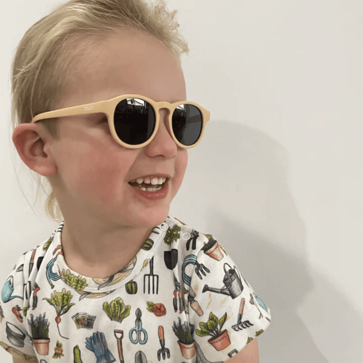 A little girl wearing Zazi Shades Baby & Toddler sunglasses by Zazi, providing UV400 protection and polarized clarity, paired with a t-shirt.