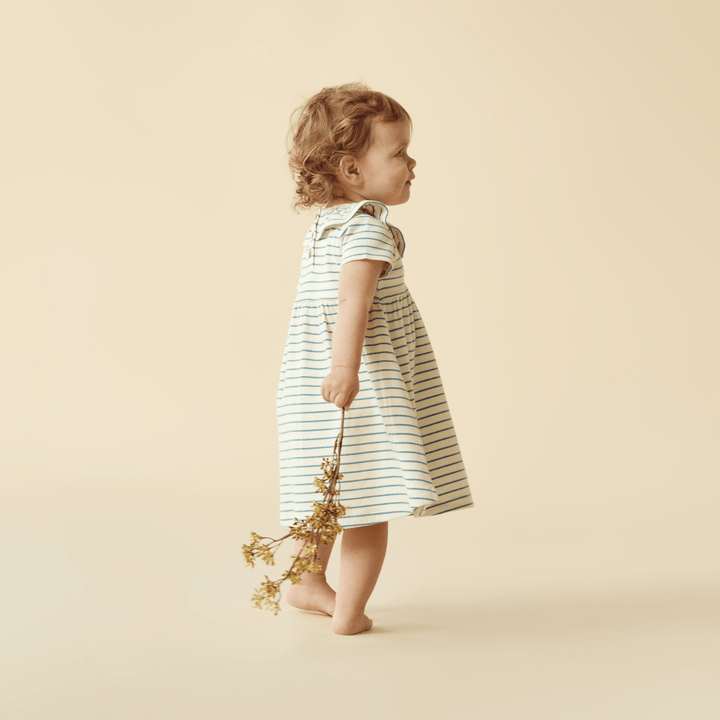 A baby girl in a Wilson & Frenchy Organic Stripe Rib Kids Ruffle Dress made of organic cotton.