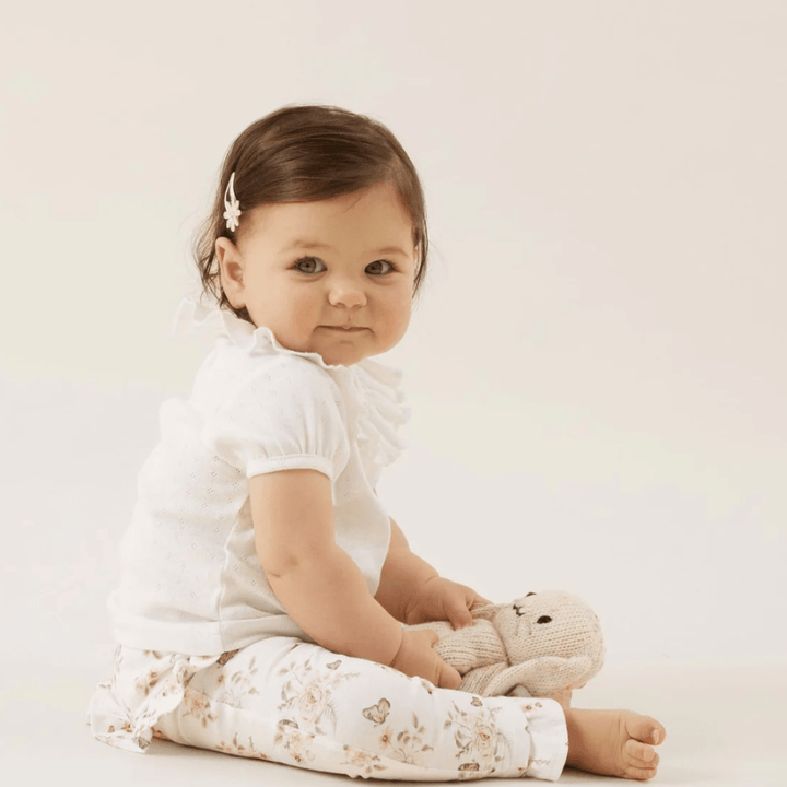 An adorable baby girl sitting on the floor with an Aster & Oak GOTS-certified organic cotton teddy bear.
