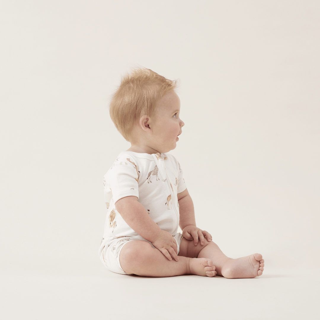 A baby sitting on the floor in an Aster & Oak Organic Cotton Zip Romper.