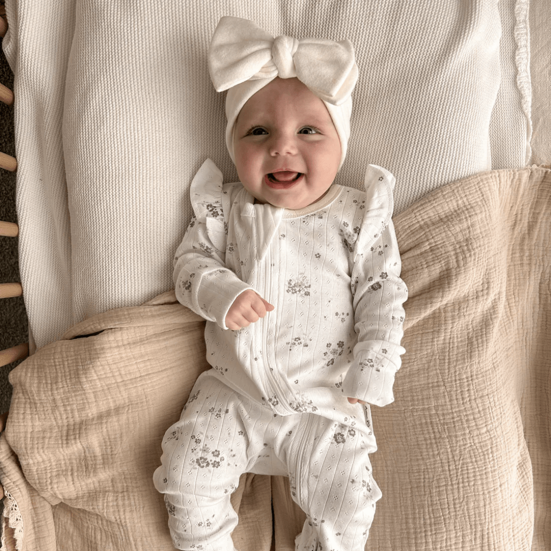 Smiley-Baby-Wearing-Aster-And-Oak-Organic-Grace-Floral-Long-Sleeve-Zip-Romper-With-Big-Bow-Headband-Naked-Baby-Eco-Boutique