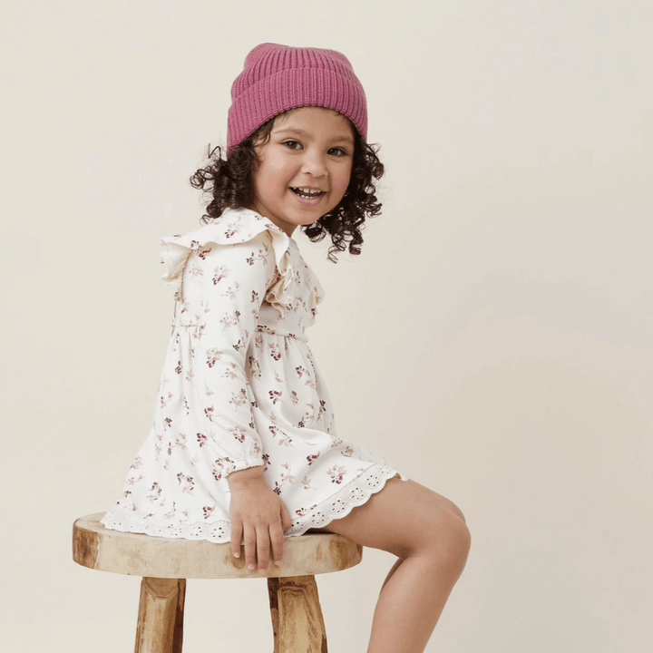 Smiling-Child-Sitting-on-Stool-Wearing-Aster-and-Oak-Organic-Cotton-PomPom-Beanie-Berry-Naked-Baby-Eco-Boutique