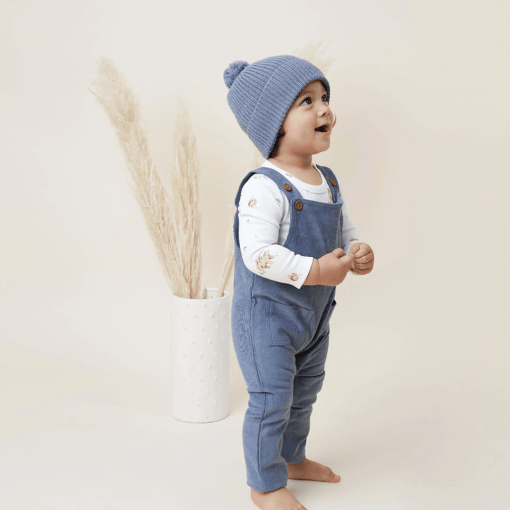 Smiling-Child-in-Overalls-Wearing-Aster-and-Oak-Organic-Cotton-PomPom-Beanie-Navy-Naked-Baby-Eco-Boutique