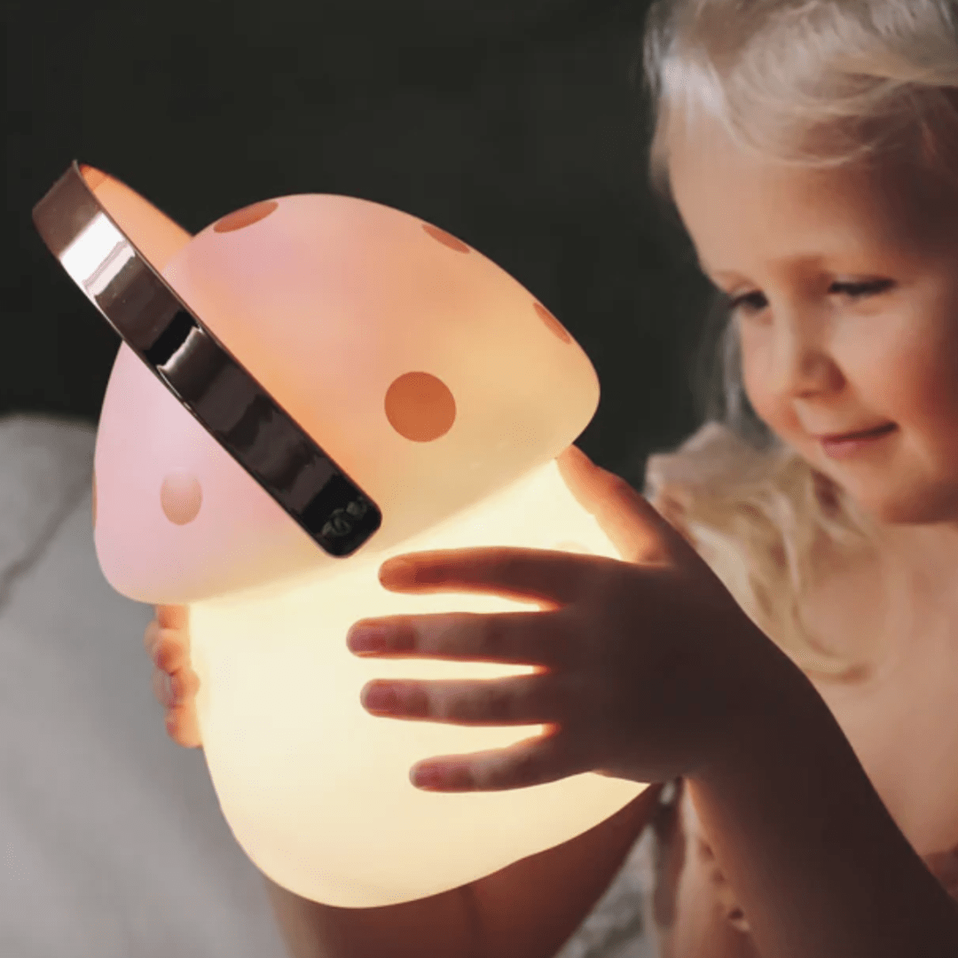 A little girl holding up a pink Little Belle Nightlights Fairy House Carry Lantern, resembling a mushroom.