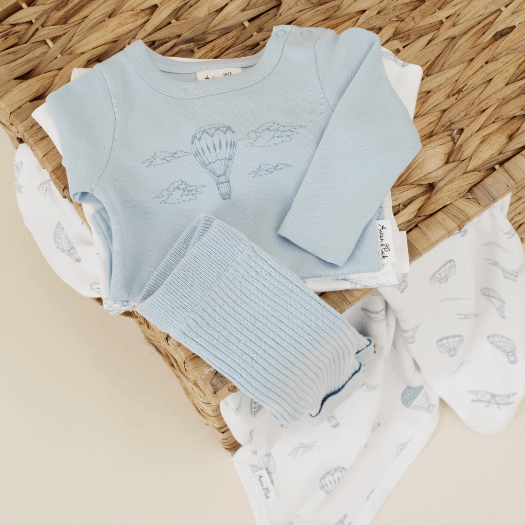 Baby bodysuit with an Aster & Oak Organic Air Balloon Long-Sleeved Onesie motif arranged on a wicker surface.