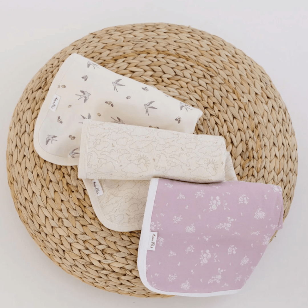 A set of three Aster & Oak Organic Cotton Baby Swaddle Wraps, elegantly hand-illustrated with a charming print, presented in a wicker basket.