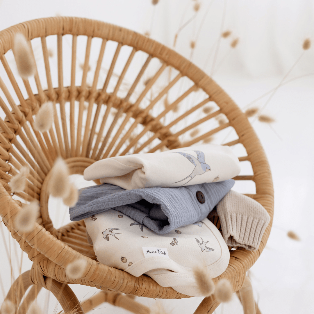 An Aster & Oak Organic Cotton Baby Swaddle Wrap with clothes on it, featuring a hand-illustrated print.