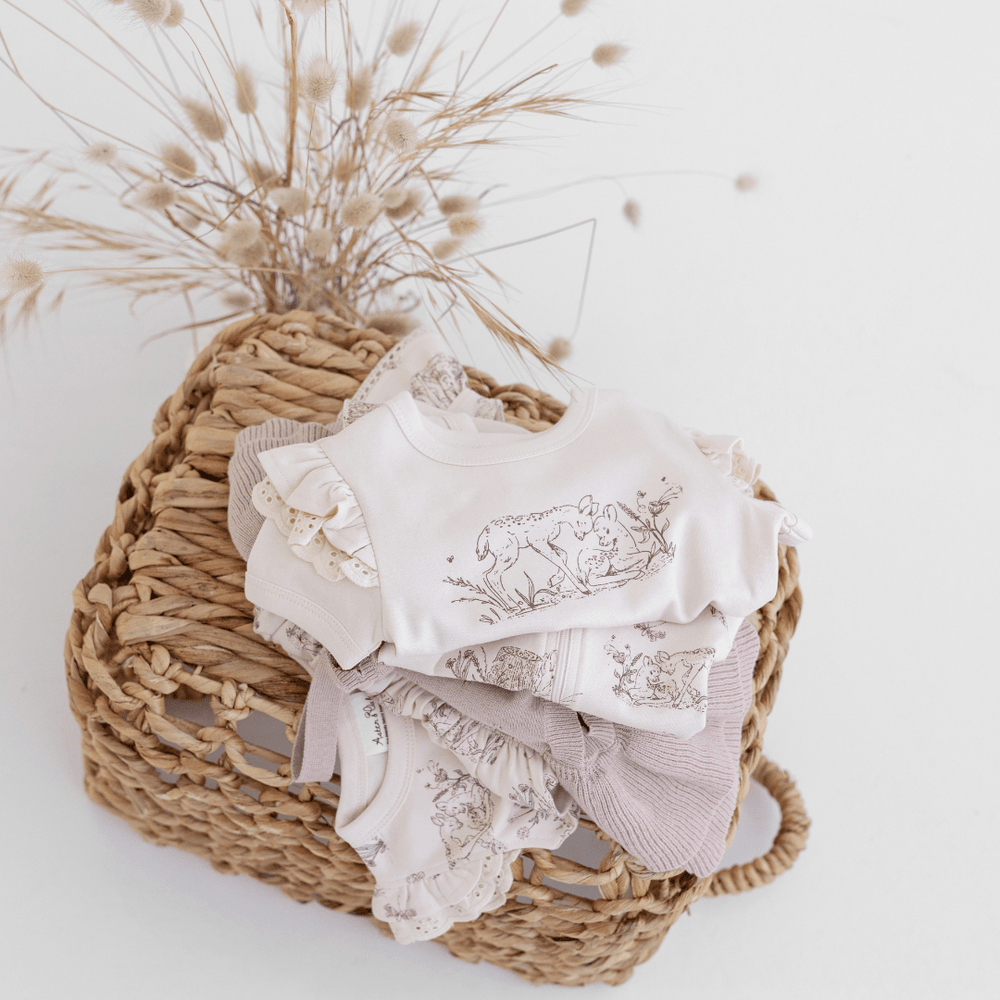 A wicker basket with an Aster & Oak Organic Cotton Fawn Print Flutter Tee in organic cotton.