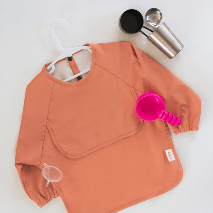 A Zazi Recycled Full-Sleeved Bib (Multiple Variants) with a pink cup and spoon.