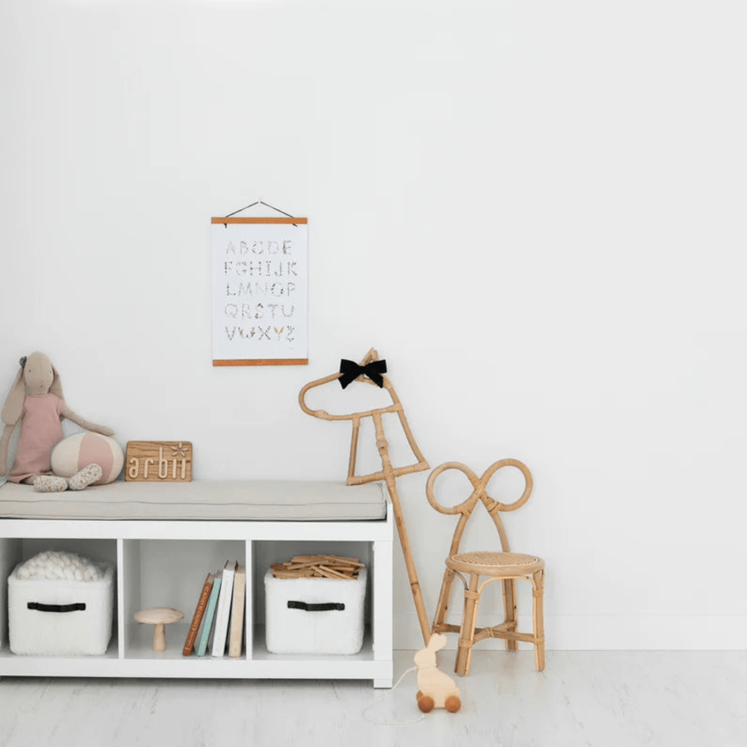 A child's room with a wooden bench, a giraffe, a teddy bear, and an eco-responsible Classical Child Rattan Hobby Horse for imaginative fun.