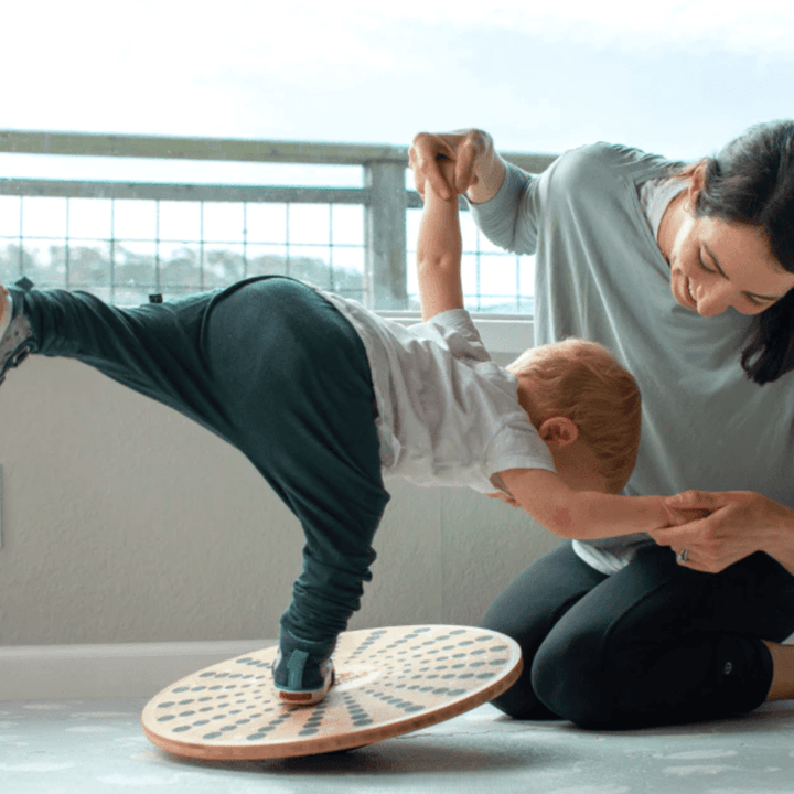 A woman and a child engaging in sustainable fitness on a Kinderfeets Bamboo Balance Disk to strengthen muscles.