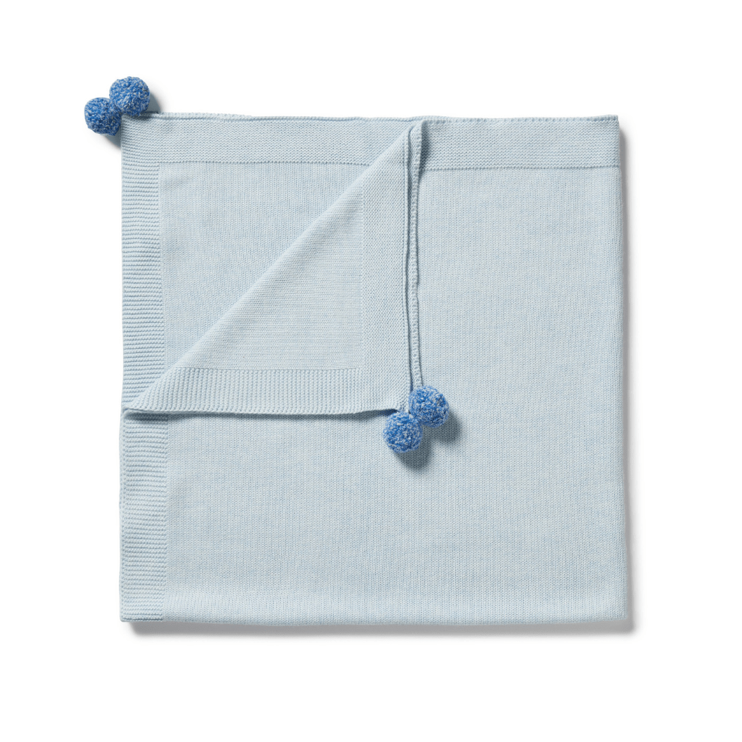 Light blue cotton Wilson & Frenchy knitted baby blanket with pom-pom details on white background.