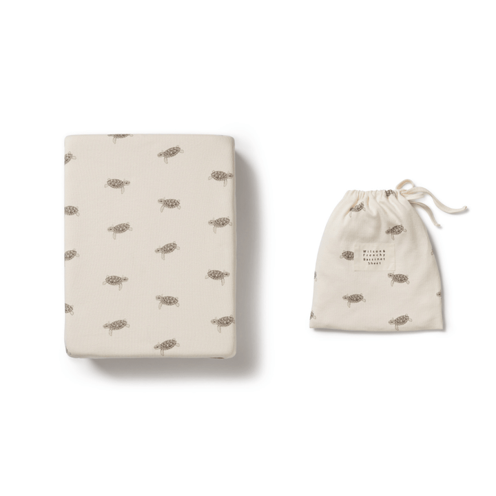Folded Wilson & Frenchy organic rib bassinet sheet in Lucky Lasts - Shine On Me & Summer Days Only with tortoise patterns next to a matching Wilson & Frenchy drawstring bag on a white background.