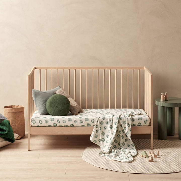 A baby's room with a wooden crib and Wilson & Frenchy Organic Baby Swaddle Blanket - LUCKY LAST - TROPICAL GARDEN ONLY bedding.