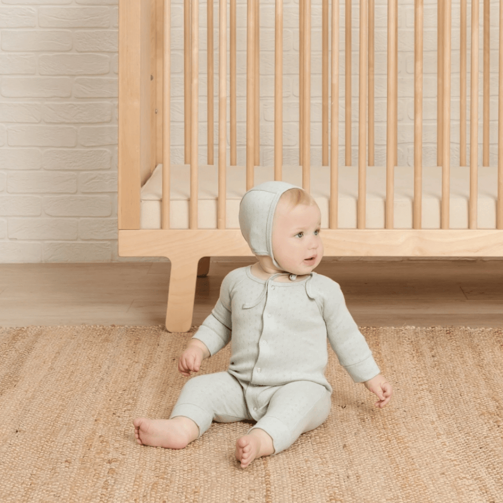 Adorable-Baby-Sitting-By-Cot-Wearing-Quincy-Mae-Organic-Cotton-Pointelle-Bonnet-Naked-Baby-Eco-Boutique