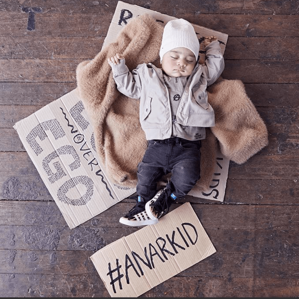 Product description: A baby laying on a wooden floor with signs, featuring Anarkid Organic Cotton Knitted Beanie (Multiple Variants) and final sale.