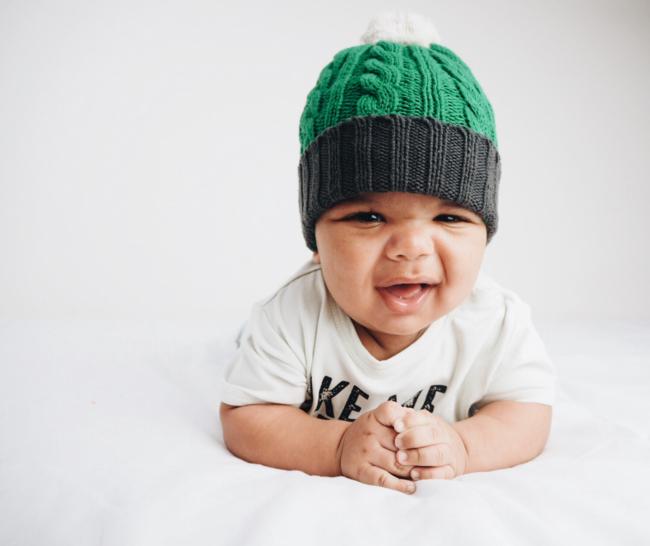 An Anarkid baby, wearing an Anarkid Organic Cotton Knitted Beanie (Emerald), is peacefully laying on a bed.