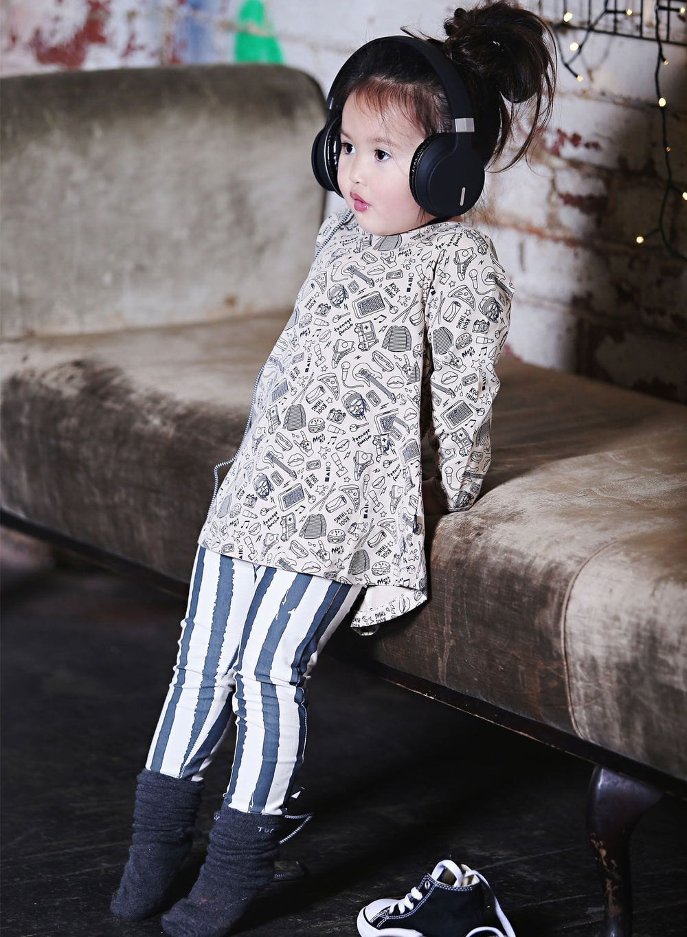 A little girl wearing Anarkid Organic Cotton Mosh Pit Band Swing Dress - LUCKY LAST - 0-3 MONTHS and sitting on a couch, ethically made.