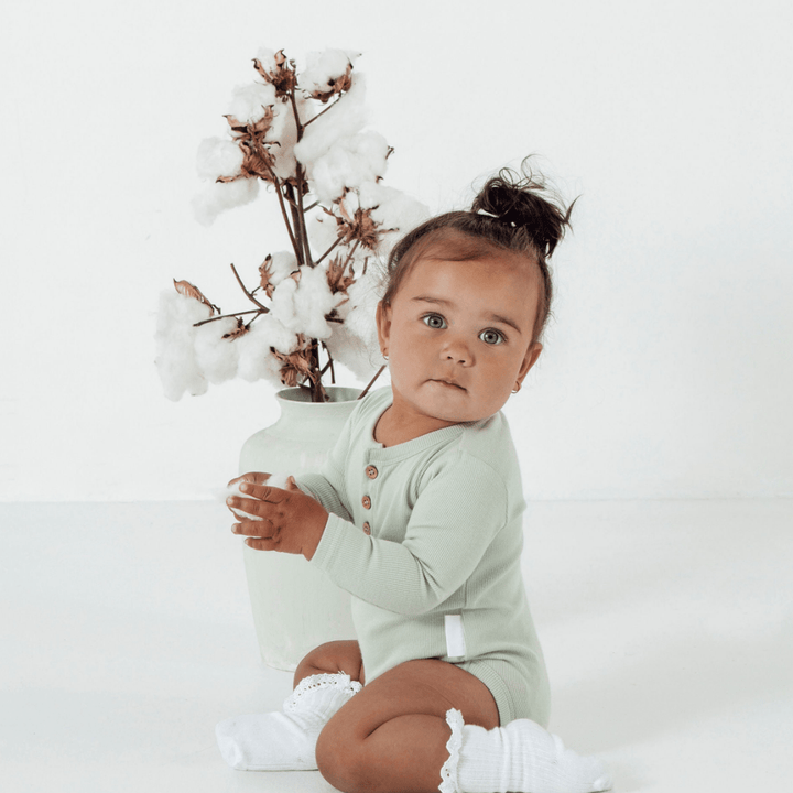 Baby-Girl-Holding-Cotton-Wearing-Aster-and-Oak-Organic-Rib-Onesie-Seafoam-Naked-Baby-Eco-Boutique