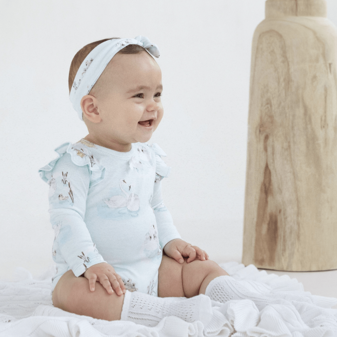 Baby-Girl-Sitting-Wearing-Aster-and-Oak-Organic-Print-Flutter-Onesie-Swan-Naked-Baby-Eco-Boutique