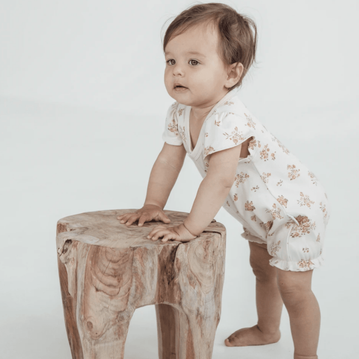 Baby-Leaning-on-Stool-Wearing-Aster-and-Oak-Organic-Posy-Floral-Ruffle-Romper-Naked-Baby-Eco-Boutique