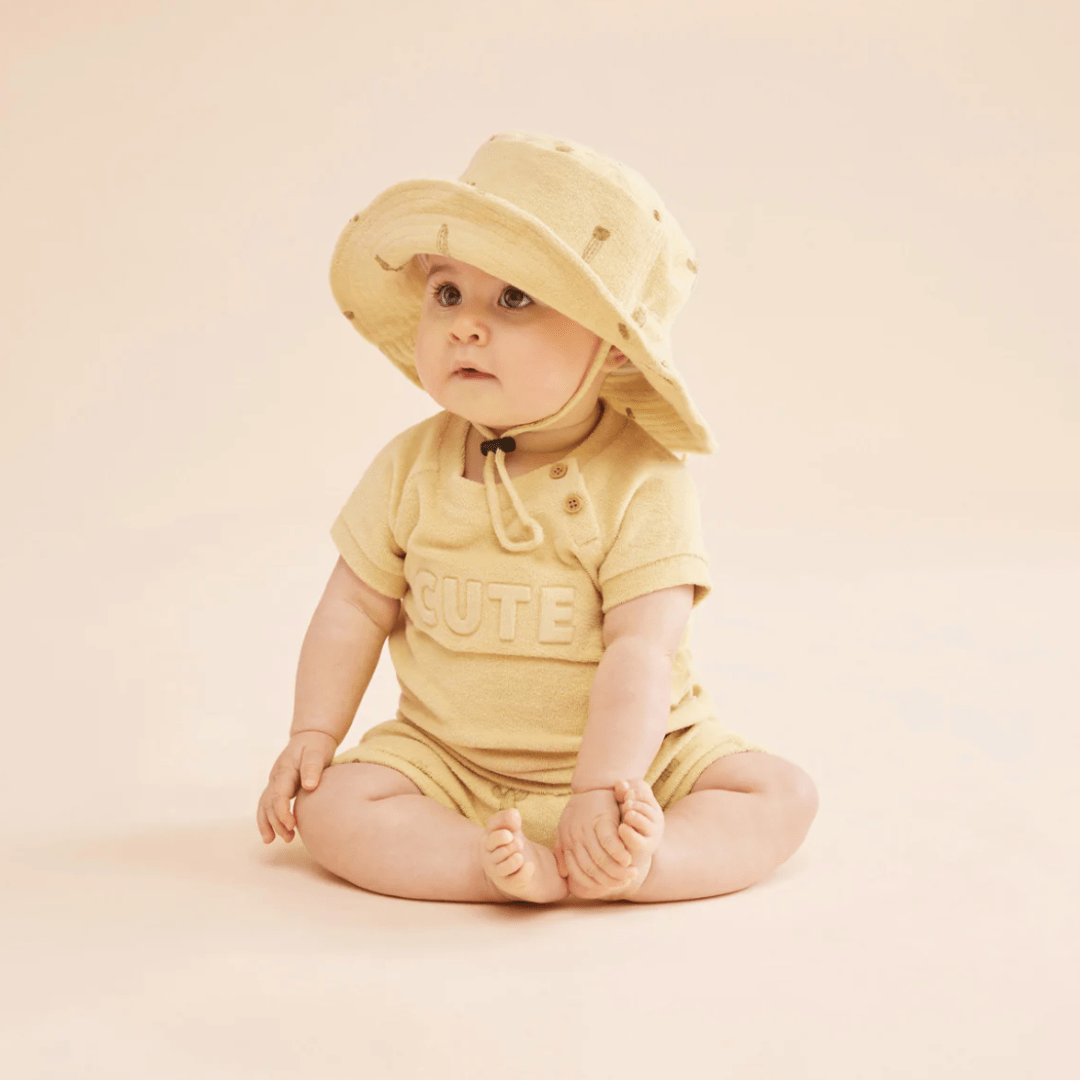Baby-Looking-to-Side-Wearing-Baby-Sitting-Wearing-Sunhat-and-Wilson-and-Frenchy-Organic-Terry-Tie-Front-Shorts-Prickle-Naked-Baby-Eco-Boutique
