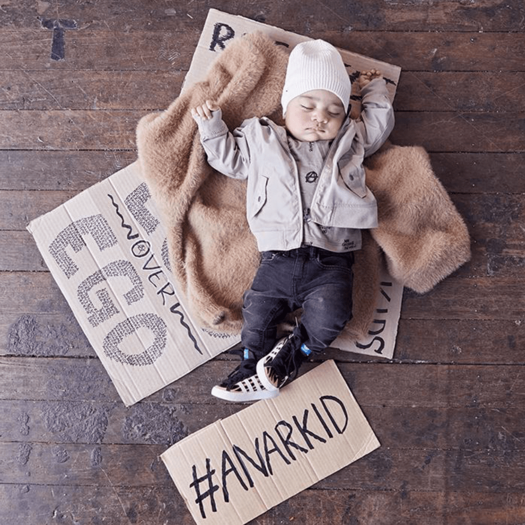 A unisex baby laying on a wooden floor wearing an Anarkid Bomber Jacket - LUCKY LAST - NAVY - 0-3 MONTHS.