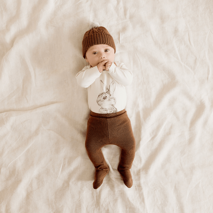 Baby-Lying-Down-Wearing-Wilson-and-Frenchy-Cable-Knit-Hat-Dijon-with-Bunny-Onesie-Naked-Baby-Eco-Boutique