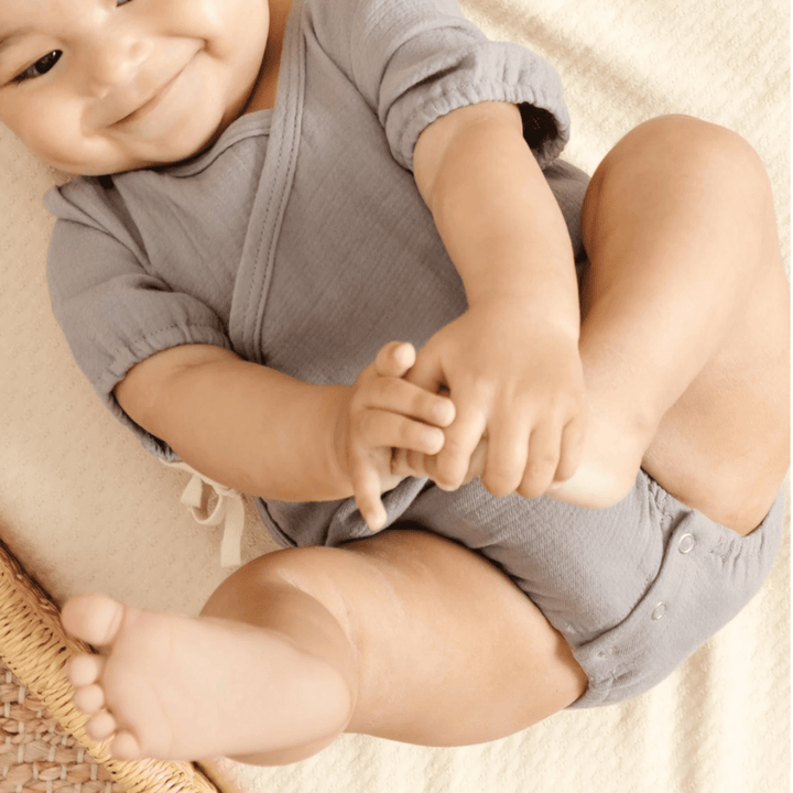 Baby-Smiling-Playing-with-Feet-Wearing-Quincy-Mae-Organic-Cotton-Woven-Wrap-Onesie-Washed-Indigo-Naked-Baby-Eco-Boutique