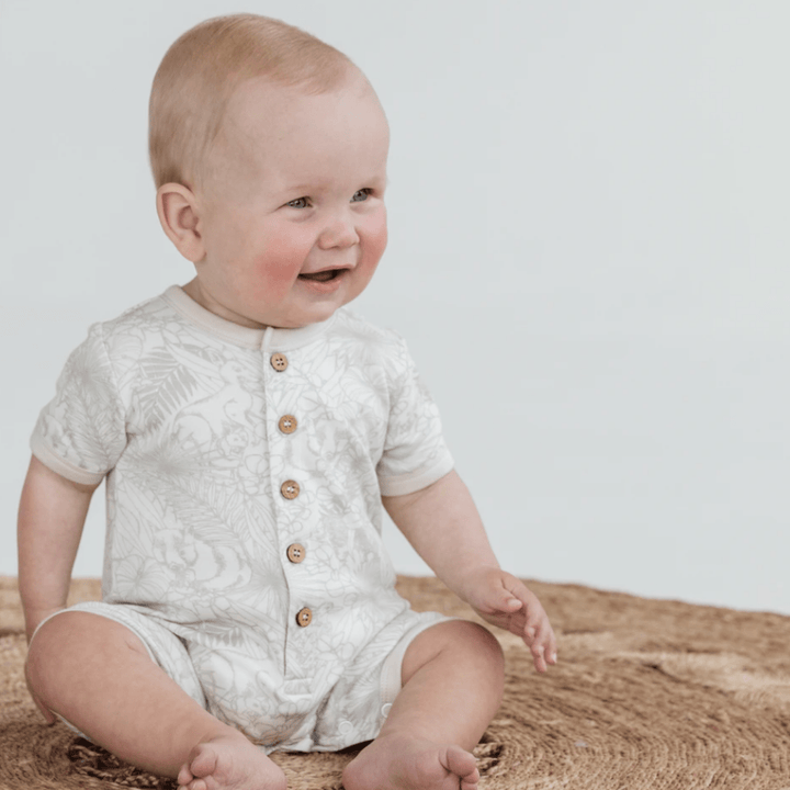 A baby in an Aster & Oak Organic Animal Button Romper - LUCKY LASTS - NEWBORN sitting on a rug.