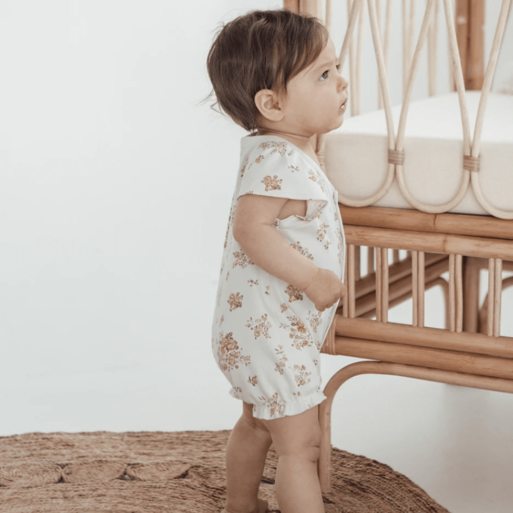 Baby-Standing-by-Cot-Wearing-Aster-and-Oak-Organic-Posy-Floral-Ruffle-Romper-Naked-Baby-Eco-Boutique