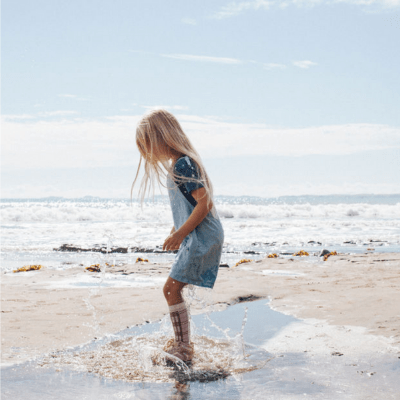 A little girl playing in the sand at the beach while wearing Lamington Merino Wool Knee-High Socks - LUCKY LAST - CARNIVAL - 2-4 YEARS ONLY that stay on her feet.