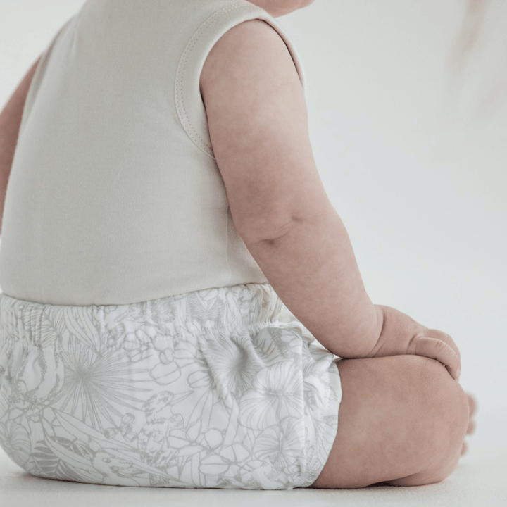 A baby is sitting on the floor in Aster & Oak Organic Animal Bloomers.