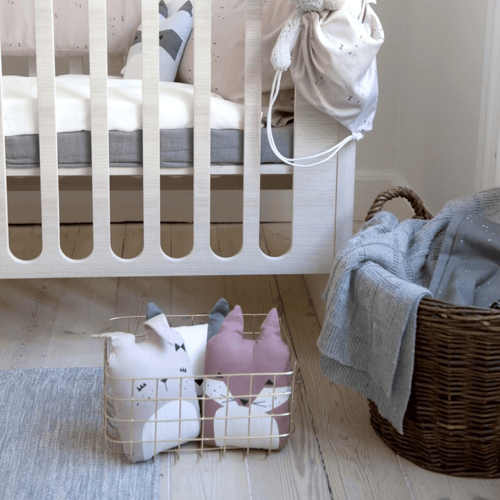 A baby's room with a white crib, a basket, and Fabelab Organic Cotton Animal Cushions - LUCKY LAST - BEAR (HONEY) bedding.