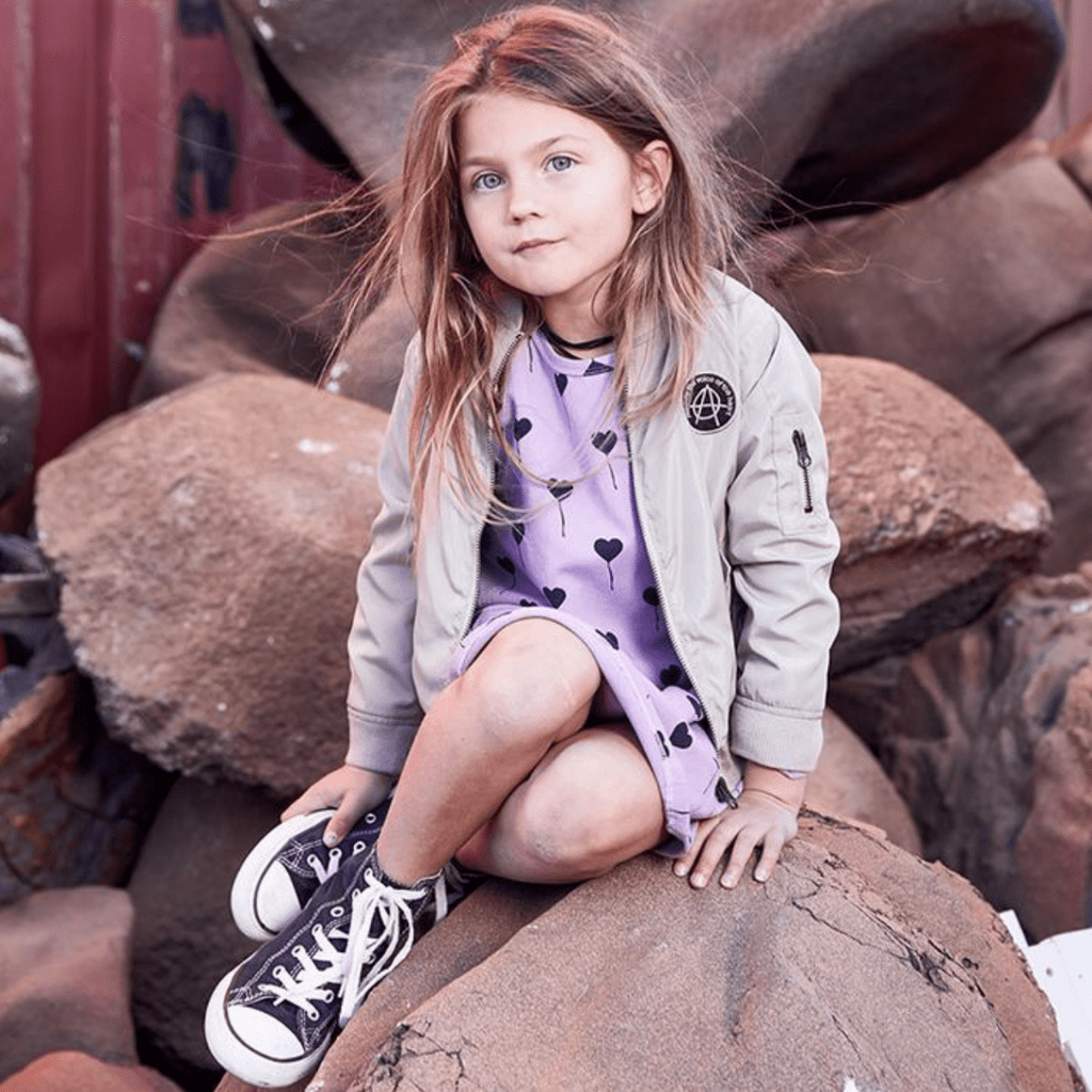 A little girl is sitting on rocks and wearing the Anarkid Bomber Jacket - LUCKY LAST - NAVY - 0-3 MONTHS.