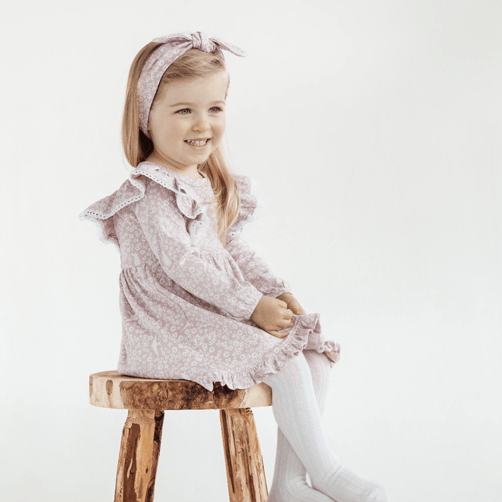 Smiling-Girl-Sitting-on-Stool-Wearing-Aster-and-Oak-Organic-Cotton-Headband-Pixi-Floral-Naked-Baby-Eco-Boutique