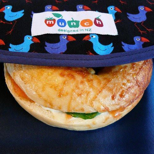 A sustainable Munch Reusable Lunch Wrap - LUCKY LASTS - KIWI ONLY rests on a blue fabric with bird patterns and a label reading 'munch, designed in nz'.
